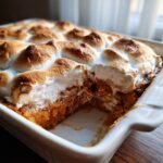 A close-up of a sweet potato casserole with a golden-brown toasted marshmallow topping in a white baking dish.