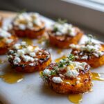 Close-up of sweet potato rounds topped with crumbled feta cheese, drizzled with honey, and garnished with fresh thyme.