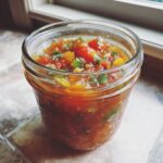 A close-up of a glass jar filled with vibrant homemade tomato salsa, showcasing chunks of tomatoes, peppers, and herbs.