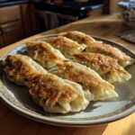 A plate of golden-brown, pan-fried Traditional Chinese Dumplings with crispy bottoms, ready to be enjoyed.