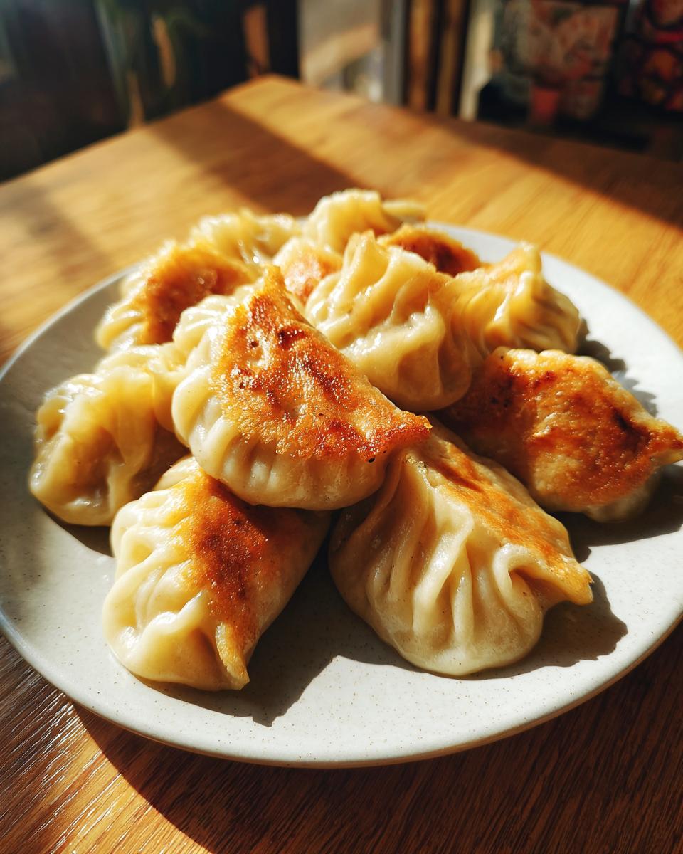 A plate of golden-brown pan-fried Traditional Chinese Dumplings, showcasing their pleated tops and crispy bottoms.