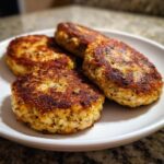 Close-up of four golden brown, pan-fried tuna patties served on a white plate.