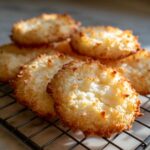 Close-up of golden-brown whipped shortbread cookies with shredded coconut texture on a cooling rack.