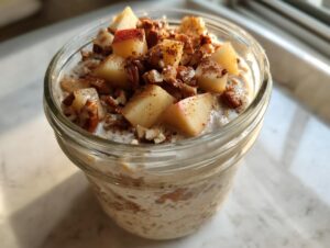 Close-up of apple cinnamon overnight oats topped with diced apples, pecans, and cinnamon in a glass jar.