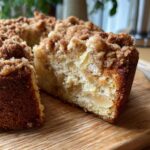 Close-up of a slice of moist apple crumb cake with visible apple pieces and a crunchy crumb topping.