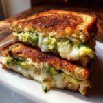 Close-up of a perfectly grilled avocado mozzarella grilled cheese sandwich, oozing with melted cheese and fresh avocado.