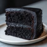 Close-up of a moist slice of black velvet halloween cake with dark chocolate frosting on a light plate.