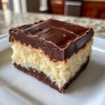 A rich slice of Boston Cream Pie Fudge with layers of chocolate and creamy filling, topped with smooth chocolate ganache.