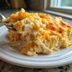 A spoonful being lifted from a serving of cheesy chicken and rice casserole topped with melted cheddar.