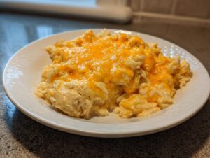 A close-up of a serving of creamy cheesy chicken and rice topped with melted bright orange cheddar cheese on a white plate.
