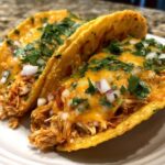 Two delicious chicken tacos filled with shredded chicken, melted cheese, diced red onion, and cilantro.
