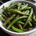 A bowl of vibrant Chinese green beans coated in a glistening garlic sauce and sprinkled with sesame seeds.