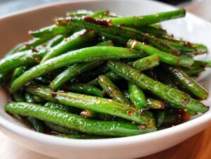 Close-up of glossy Chinese green beans coated in a savory garlic sauce, ready to be served.