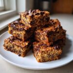 A stack of rich, chewy chocolate chip oat bars, ideal as sweet snacks, piled on a white plate.