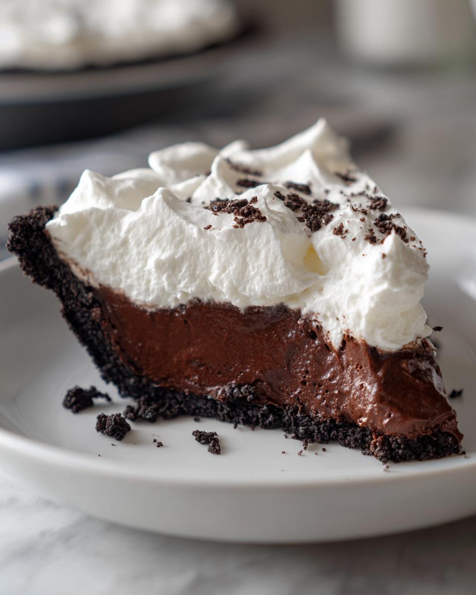 A decadent slice of Christmas chocolate cream pie featuring a dark chocolate filling, Oreo crust, and fluffy whipped cream topping.