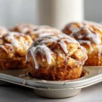 Close-up of freshly baked cinnamon roll bites drizzled with white glaze in a muffin tin.