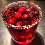 A close-up of a festive Cranberry Pomegranate Margarita, garnished with fresh cranberries and a salted rim.