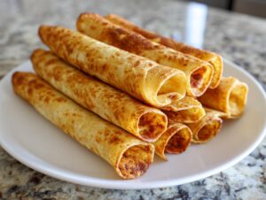 A stack of golden, crispy cream cheese chicken taquitos served on a white plate.