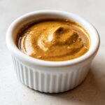 Close-up of rich, creamy peanut sauce texture served in a small white fluted ramekin.