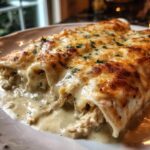 Close-up of baked creamy queso chicken enchiladas oozing sauce and topped with browned cheese and parsley.