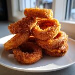 A tall stack of perfectly golden brown, crispy onion rings piled high on a white plate.