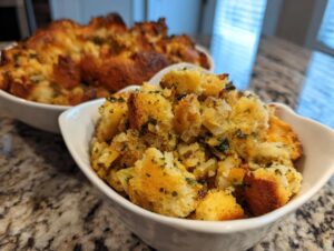 Close-up of golden brown crock pot stuffing with herbs served in white bowls.
