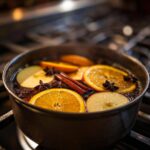 Close-up of ingredients for fall simmering potpourri, including orange slices, apple slices, cinnamon sticks, and star anise simmering in water.