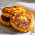 A close-up of a stack of golden-brown fried cornbread hoecakes on parchment paper.
