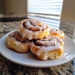 Close-up of four glazed cinnamon roll cookies stacked on a white plate, ready to eat.