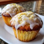Two freshly baked lemon poppy seed muffins topped with thick white glaze and lemon zest.