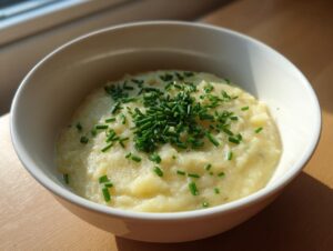 A white bowl filled with thick, creamy high protein cream of potato soup, topped generously with fresh chopped chives.