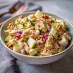 A bowl of delicious Honey Mustard Chicken Salad with chunks of apple, red onion, and walnuts, garnished with parsley.
