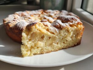A slice of moist Italian apple cake, studded with apple pieces and dusted with powdered sugar, served on a white plate.