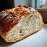 Close-up of a freshly baked Italian bread slice showing a golden, crackly crust and an airy, open crumb structure.