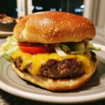A close-up of a juicy burger with melted cheddar cheese, fresh lettuce, and tomato slices on a sesame seed bun.