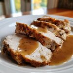 Close-up of four slices of juicy crockpot turkey breast, seasoned and topped with brown gravy, served on a white plate.