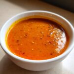 Close-up of a bowl filled with rich, orange McDonald's Cajun sauce, sprinkled with black pepper and red pepper flakes.