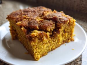 Close-up of a moist, orange slice of pumpkin dump cake with a crumbly, spiced topping on a white plate.