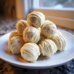 A stack of white chocolate coated No bake pumpkin cheesecake balls drizzled with extra white chocolate and sprinkled with spice.