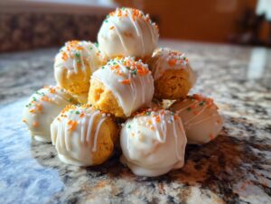 A stack of delicious Pumpkin Oreo Balls dipped in white chocolate, drizzled with more white chocolate, and topped with orange, green, and white sprinkles.