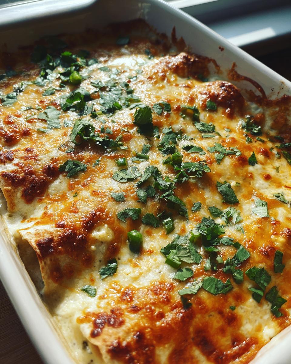 Close-up of creamy queso chicken enchiladas baked in a white dish, topped with melted cheese and fresh cilantro.