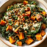 A vibrant bowl of roasted sweet potato kale salad topped with pumpkin seeds and a creamy dressing.