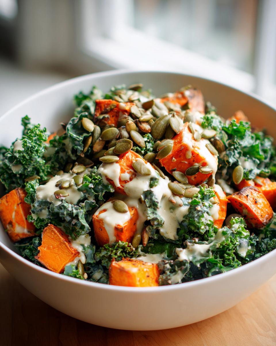 A bowl of roasted sweet potato kale salad topped with pumpkin seeds and a creamy dressing.
