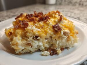 A close-up of a serving of creamy slow cooker chicken bacon ranch casserole topped with melted cheddar and crispy bacon bits.