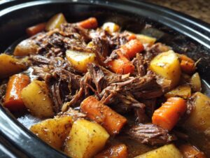 Close-up of a slow cooker pot roast with shredded beef, tender carrots, and chunks of potatoes in savory gravy.