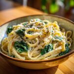 A close-up of creamy spinach alfredo pasta in a rustic bowl, topped with grated cheese and pepper.