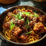 A close-up of sticky garlic chicken noodles topped with sesame seeds and sliced green onions.