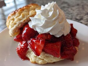A close-up of a delicious strawberry shortcake featuring a split biscuit, macerated strawberries, and a dollop of whipped cream.