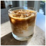 A refreshing Toasted Coconut White Russian cocktail with layers of cream and coffee, topped with toasted coconut flakes.