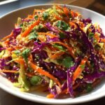 Close-up of a colorful cabbage salad featuring shredded red and green cabbage, carrots, and sesame seeds.